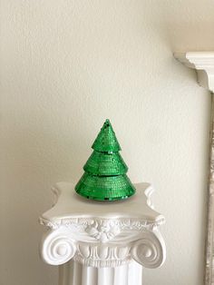 a green christmas tree sitting on top of a white pedestal in front of a wall