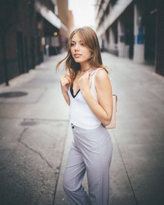 a woman is standing on the sidewalk with her hand in her pocket and looking at the camera