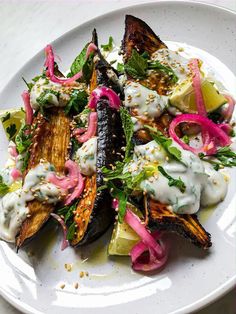 a white plate topped with an eggplant and veggie salad covered in dressing