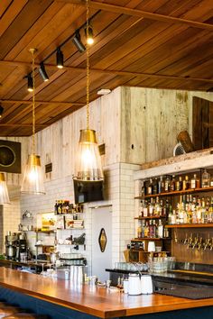 a bar with lots of bottles on the shelves and lights hanging from the ceiling above it