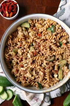 a white bowl filled with pasta and vegetables next to a small bowl of chili sauce