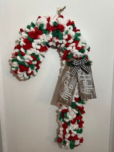 a christmas wreath hanging on the wall with two tags attached to it's sides