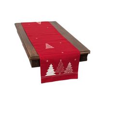 a red table runner with white christmas trees on it and a brown wooden bench in the background