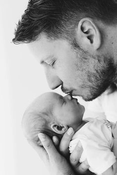 a man holding a baby in his arms and kissing it's face with the other hand