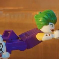 the lego batman movie character has green hair and is flying through the air with his arms outstretched