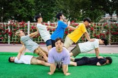 four men are doing yoga on the grass in front of flowers and fenced area