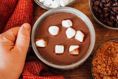 a person holding their hand over a cup of hot chocolate with marshmallows