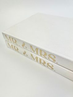 two white books with gold lettering sitting on top of each other in front of a white background