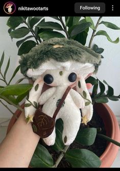 a stuffed animal in a potted plant wearing a hat and holding a pipe with leaves