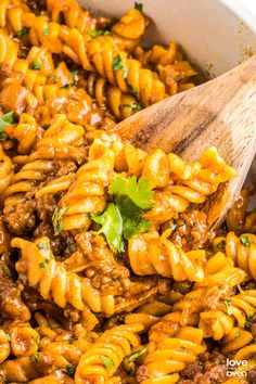 a wooden spoon in a pot full of pasta and meat sauce with parsley on top