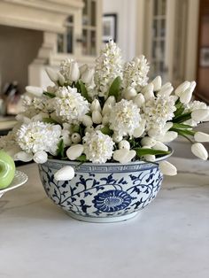 a blue and white bowl filled with flowers on top of a marble counter next to a green teapot