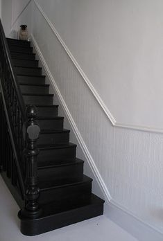 there is a black stair case on the side of this staircase with white walls and flooring