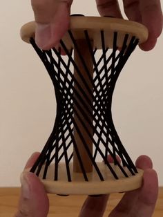 two hands are holding an object made out of wood and black wire on a wooden table