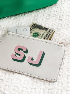 a white purse with pink and green letters sitting on top of a bed next to money