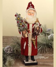 a santa clause figurine holding a christmas tree in his right hand and looking at the camera