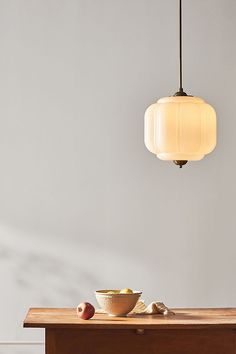 an apple sits on a table next to a bowl of fruit and a light fixture