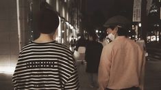 two people walking down the street at night wearing face masks and standing next to each other