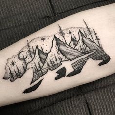 a black and white bear tattoo on the right arm with mountains in the distance behind it