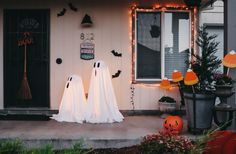 three ghost statues in front of a house decorated for halloween