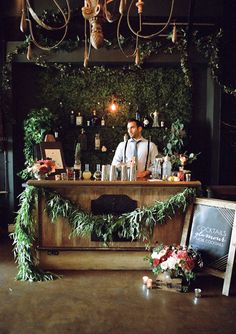 a man standing behind a bar with greenery on it