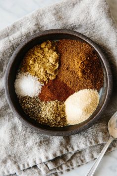 a bowl filled with spices on top of a towel next to a spoon and fork