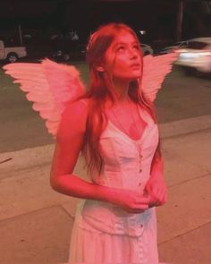 a woman in a white dress is standing on the sidewalk with an angel wings around her neck