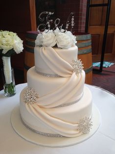 a three tiered wedding cake with white flowers on the top and initials on the side