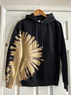 a black and gold tie - dye hoodie hangs on a white door with a wooden hanger