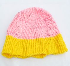 a pink and yellow knitted hat sitting on top of a white table