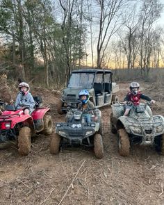 three people riding four wheelers in the woods