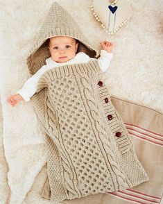 a baby wrapped up in a blanket on top of a white rug and wearing a hat