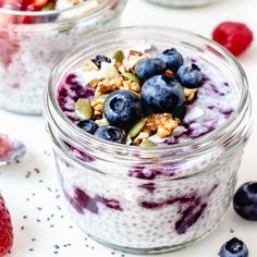 two glass jars filled with yogurt, granola and berries on a table