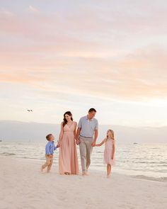 a family walking on the beach at sunset with their toddler daughter holding her dad's hand