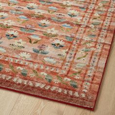 an orange rug with flowers and leaves on the top is laying on a wooden floor