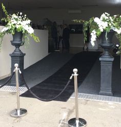 two black urns with white flowers are on display at the entrance to an event