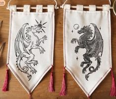 two embroidered banners hanging from hooks on a wooden table with scissors and other crafting supplies