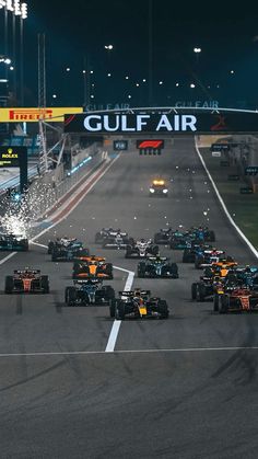 a group of racing cars driving down a race track at night with the lights on