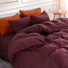 an unmade bed with red sheets and orange pillows