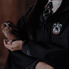 a woman in a harry potter costume holding an owl on her arm and looking at the camera