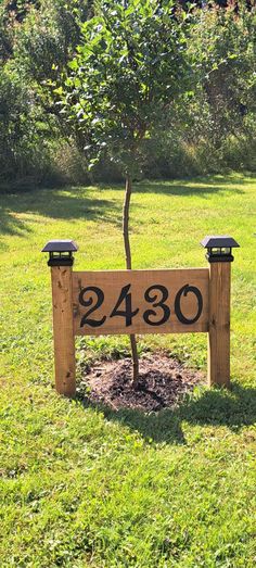 a wooden sign sitting in the middle of a field next to a tree and grass