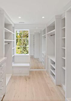 an empty walk in closet with white shelving and wood flooring on both sides