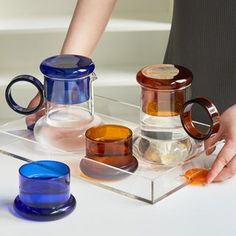 a person is holding two cups on a clear tray with different shapes and sizes in front of them