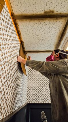 a man is working on the ceiling in his room with white and gold wallpaper