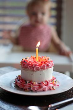 a small child sitting in a highchair behind a birthday cake with a lit candle