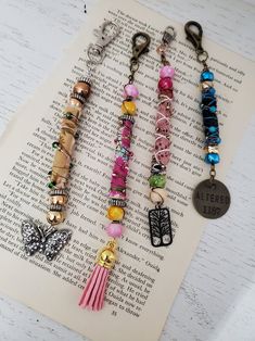 four key chains with charms on them sitting on top of an open book, next to each other