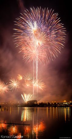 fireworks are lit up in the night sky over water and land with reflections on the water