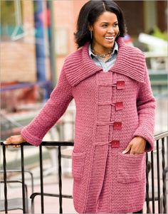 a woman standing next to a fence wearing a pink coat and smiling at the camera