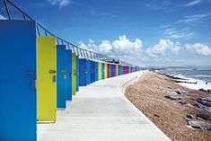 a row of brightly colored beach huts next to the ocean with blue sky and clouds