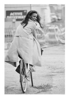 black and white photograph of a woman riding a bike in the rain wearing a coat