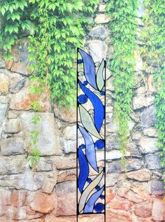 a blue and white stained glass window in front of a stone wall with ivy growing on it